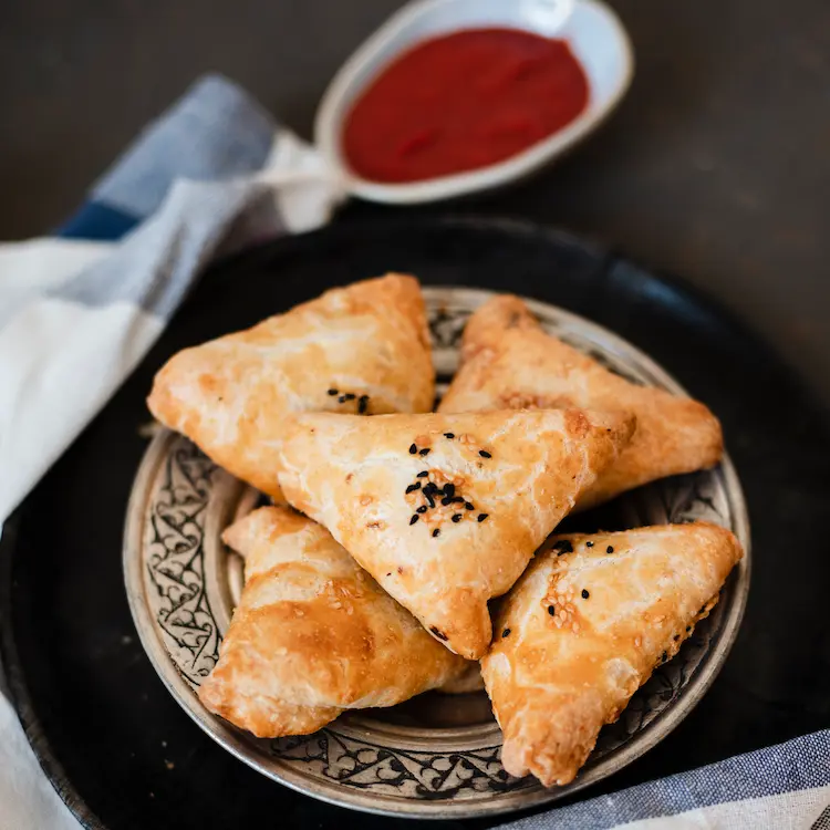 Close up shot of samosa on a white plate with red and green sauce.
