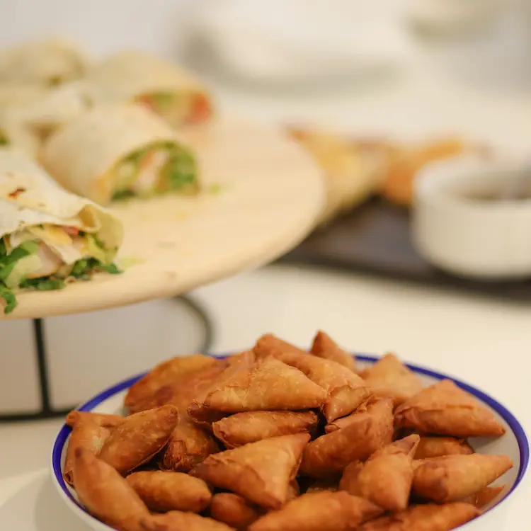 A bowl filled with mini samosas, paired with dipping sauces, set on a white table for a delicious meal.